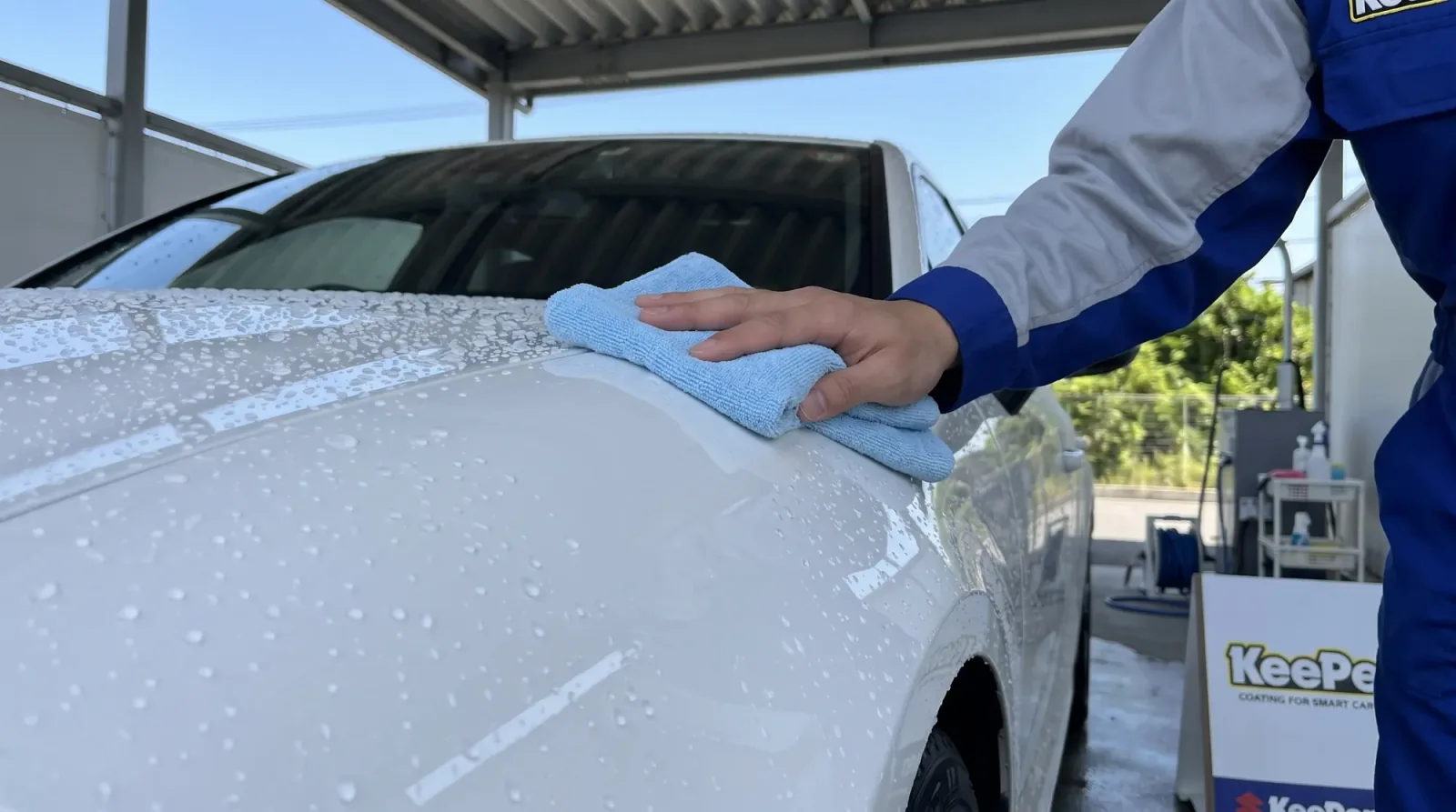 水をはじく白い車のボディを、スタッフがクロスでやさしく拭き上げている様子