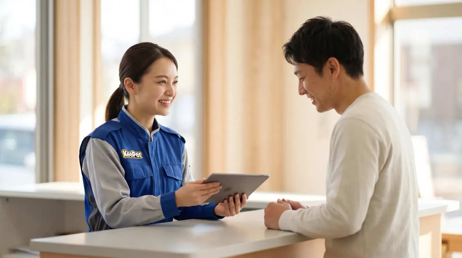 店舗のカウンターで、スタッフがタブレットを見せながらお客様にコーティングを説明している様子